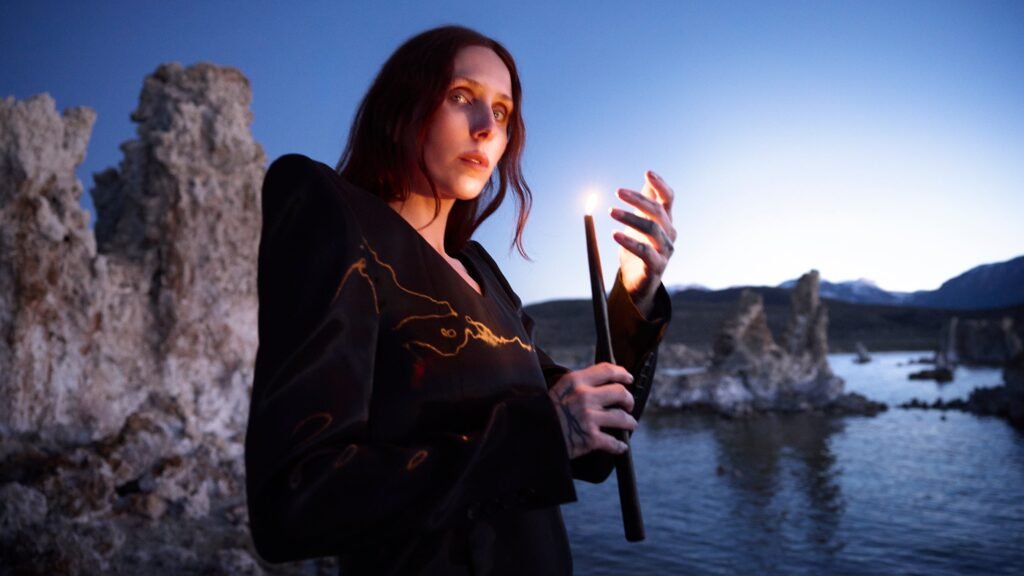 Chelsea Wolfe holds a lit candle among tufa rock formations at dusk, official press photo