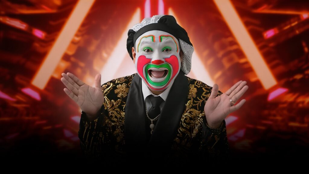 Brincos Dieras in signature clown makeup and gold ornate jacket, hands raised against red stage lighting