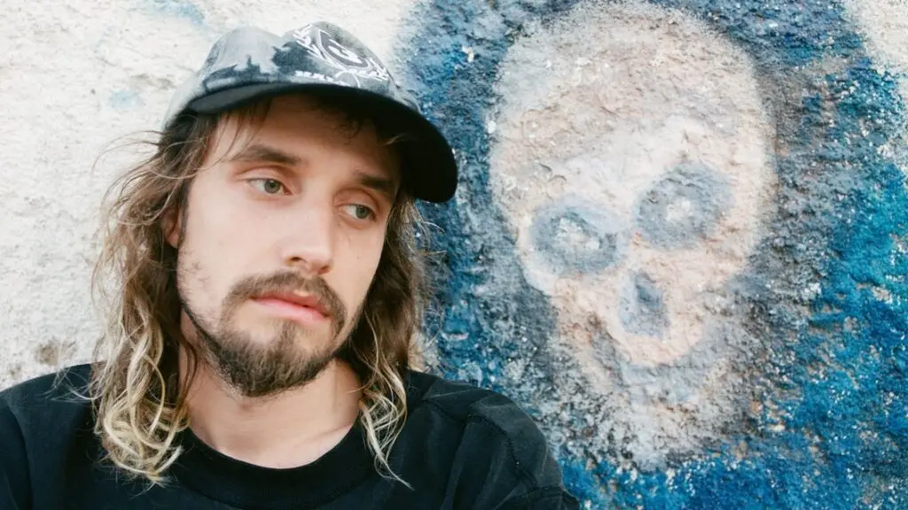 Pouya poses in front of blue skull graffiti in a press photo for The Forever Glades Tour