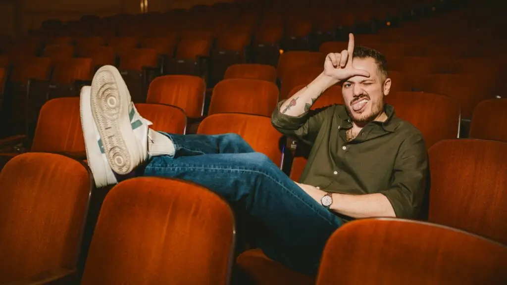 Jeff Arcuri poses in theater seats making a comedic gesture during Road Trip Tour promo shoot