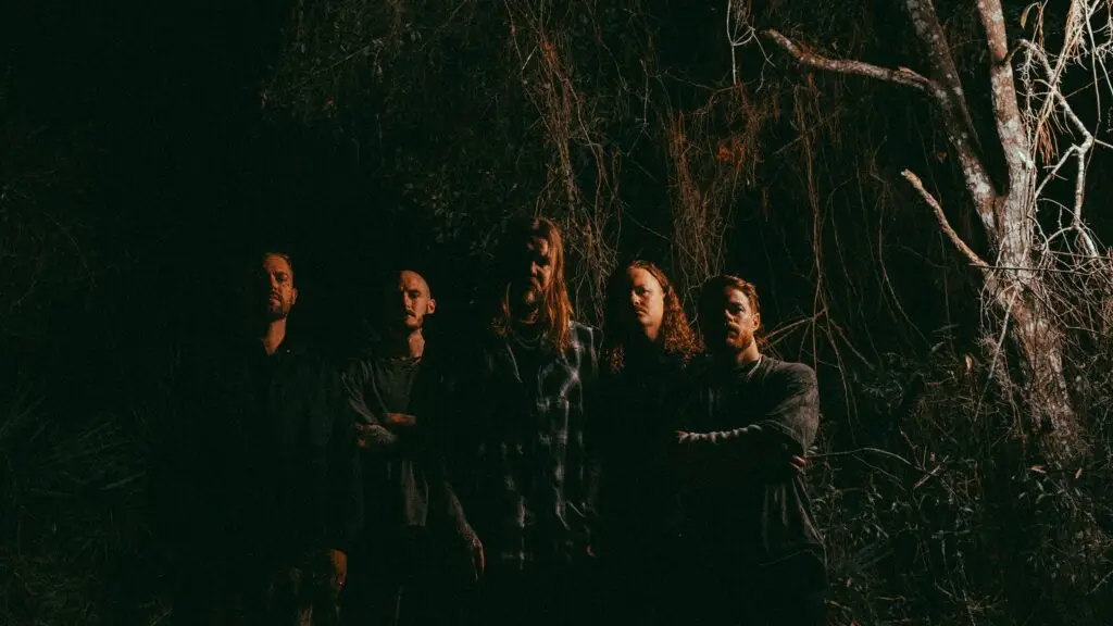 Wage War — five-piece metalcore band in dark swampy outdoor setting, bare branches background