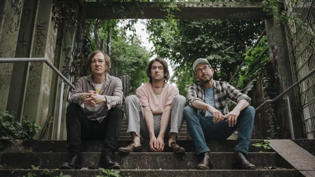 Bright Eyes — Conor Oberst, Mike Mogis, and Nate Walcott seated on outdoor stairs