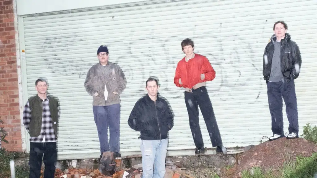 Basement band press photo, five members standing in front of a corrugated metal shutter, rainy urban setting