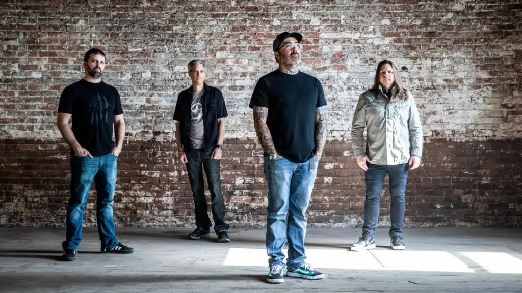 Staind band press photo — four members including Aaron Lewis standing against an exposed brick wall