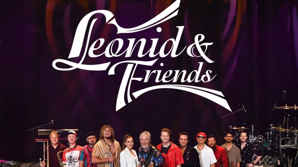 Leonid & Friends 12-piece ensemble on stage in front of purple branded logo backdrop with instruments