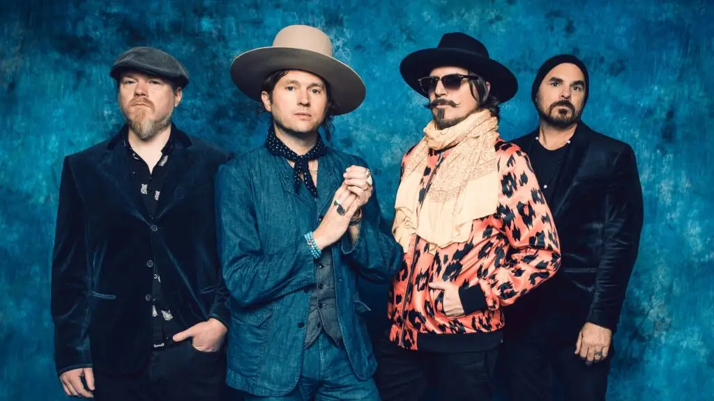 Rival Sons band press photo, four members in rock attire against blue studio backdrop