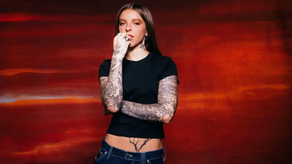 Young Miko, heavily tattooed Latin trap artist, in editorial press photo against red painted backdrop