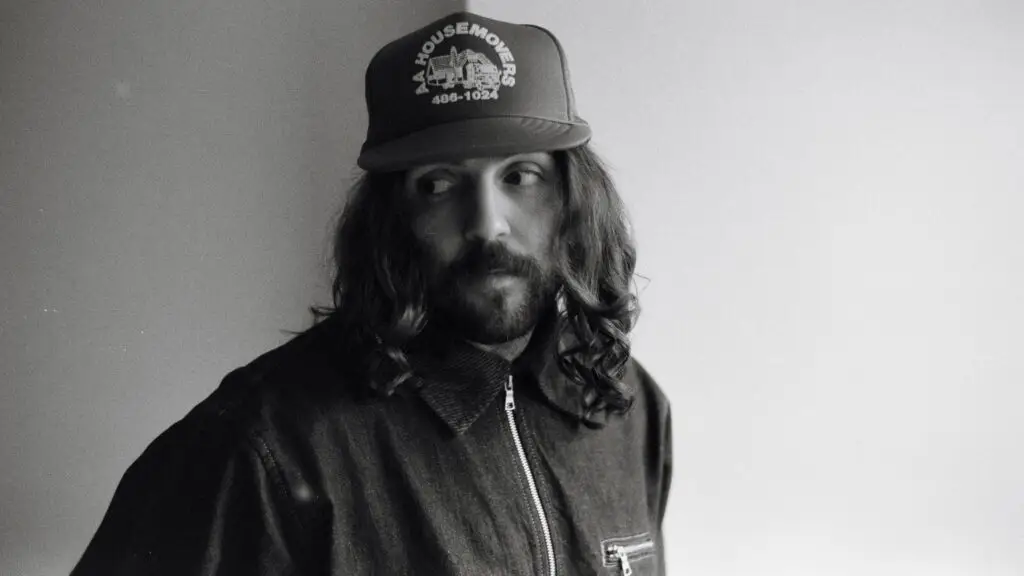 Hazlett, singer-songwriter, in a black-and-white press portrait wearing a trucker cap and denim jacket